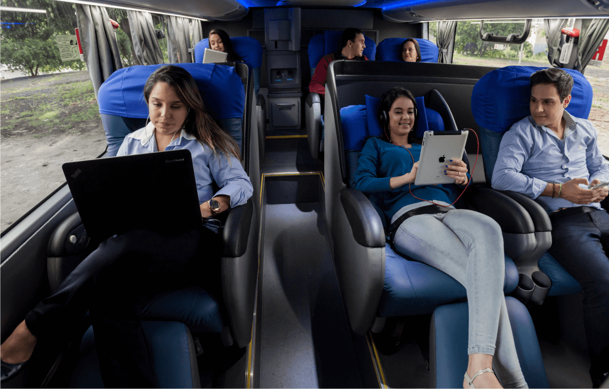 Imagem de passageiros felizes, sentados nas poltronas e aproveitando a viagem de ônibus da Águia Branca.